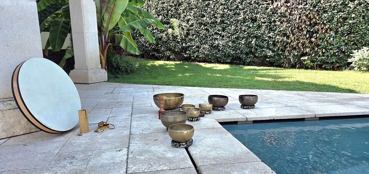 Des bols tibétains disposés sur une terrasse au bord d’une piscine, un tambour posé contre un muret, un jardin derrière