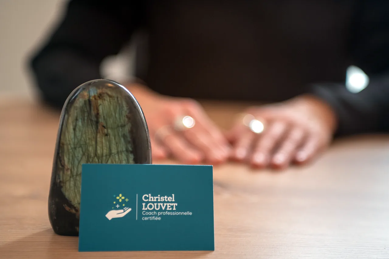 Les mains de Christel Louvet posées sur son bureau, derrière une pierre polie et sa carte de visite