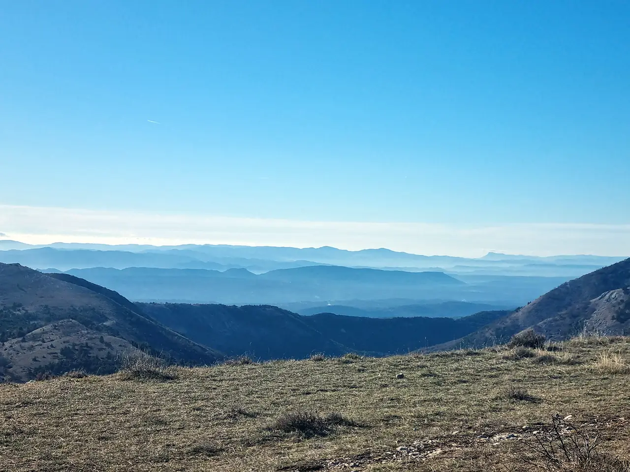 Un panorama de montagnes bleutées qui s’étagent jusqu’à l’horizon, vu depuis un plateau herbeux, photographié par Christel Louvet